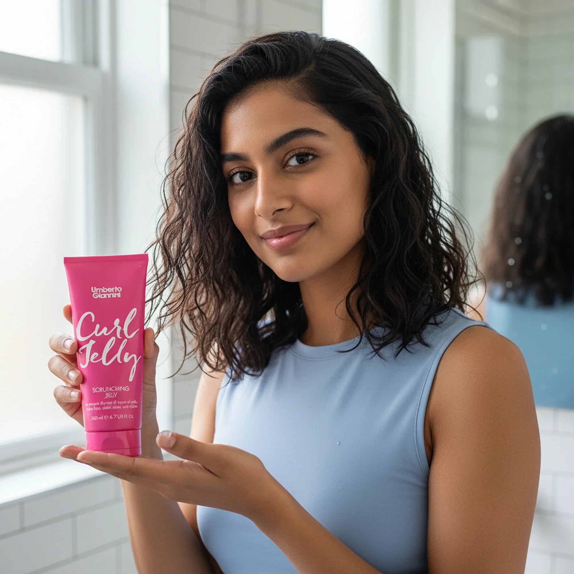 Young woman with curly hair holding Umberto Giannini Curl Jelly scrunching jelly in bathroom
