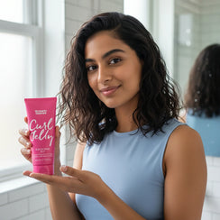 Young woman with curly hair holding Umberto Giannini Curl Jelly scrunching jelly in bathroom
