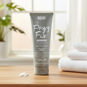 Umberto Giannini Frizz Fix conditioner tube with cream on wooden surface, white towels and plant in background