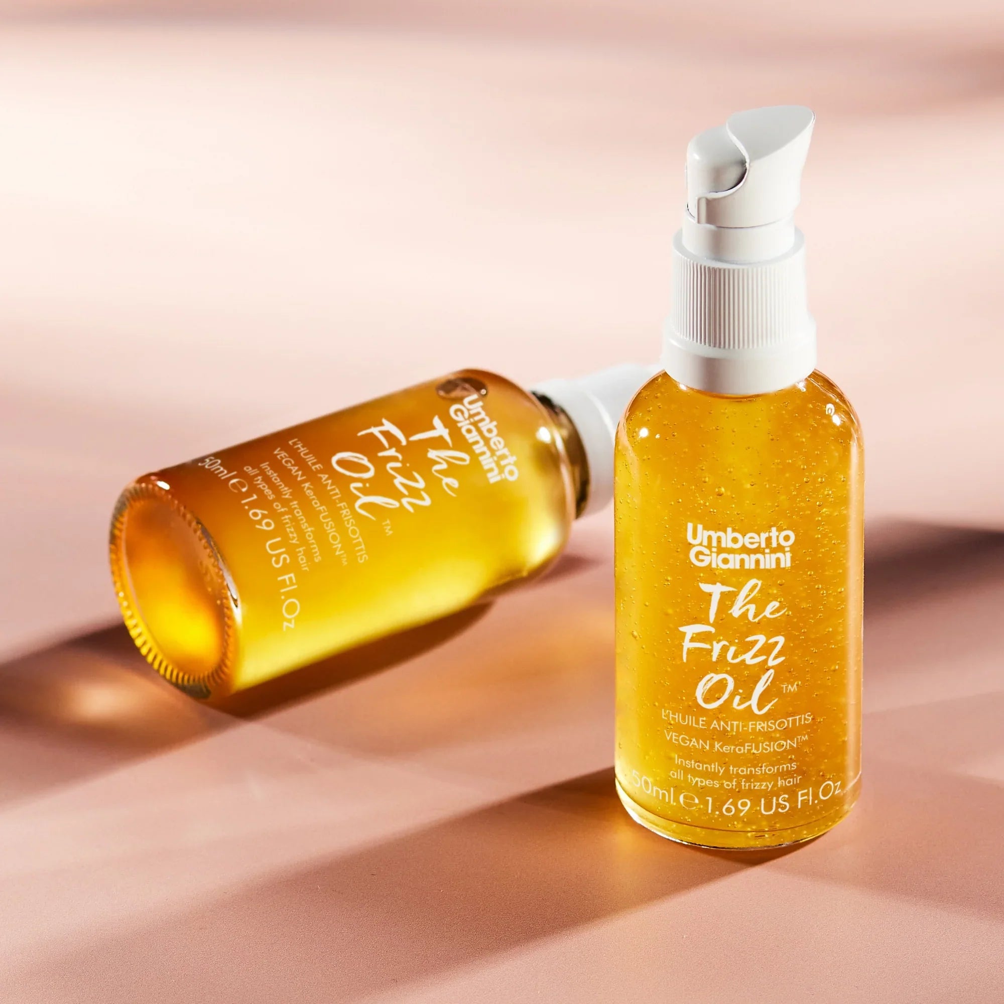Umberto Giannini The Frizz Oil vegan hair serum bottles with pump cap on pink background