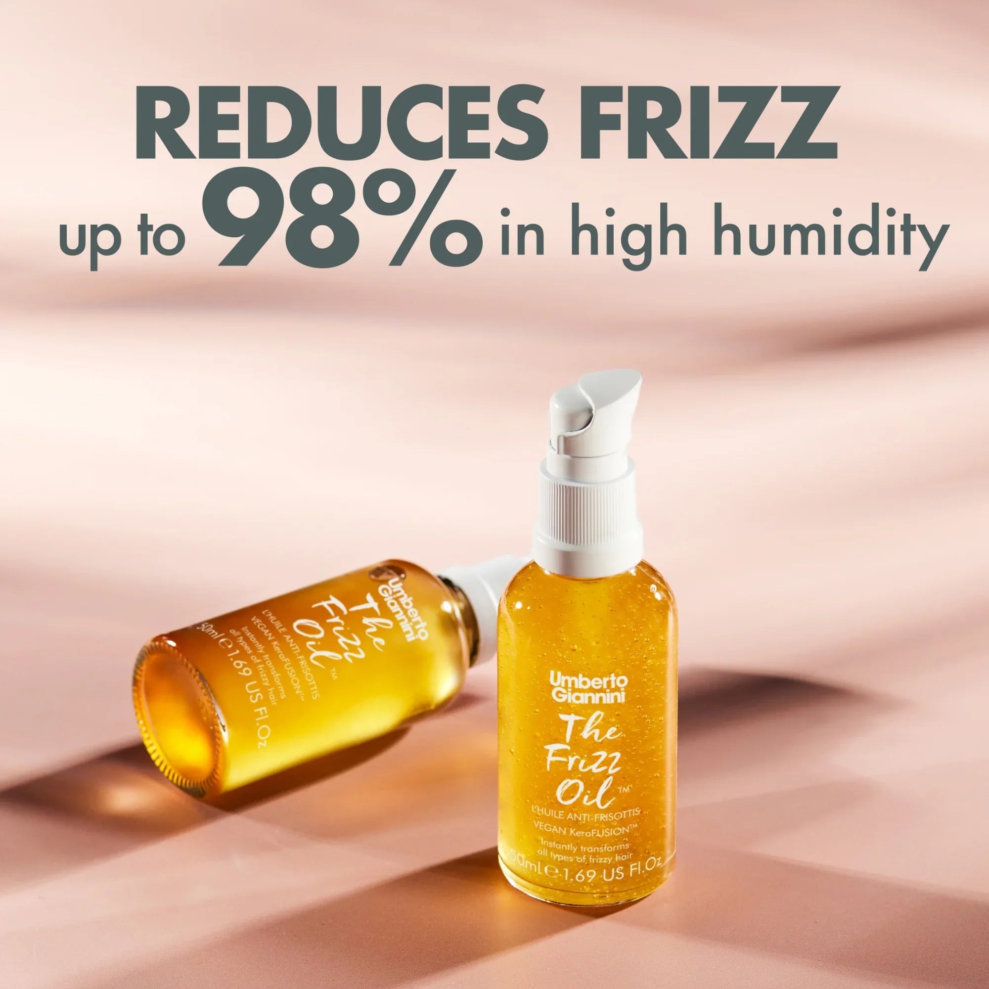 Two bottles of Umberto Giannini The Frizz Oil on a soft pink background with text reducing frizz up to 98%