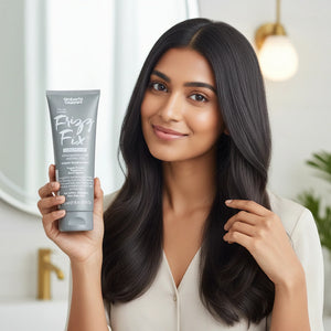 Woman with smooth black hair holding Umberto Giannini Frizz Fix conditioner in a modern bathroom