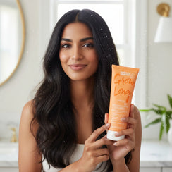 Woman with long black hair holding Umberto Giannini Grow Long hair lengthening shampoo in bright room