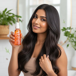 Smiling woman with long shiny black hair holding Umberto Giannini Grow Serum bottle in bright room with plants