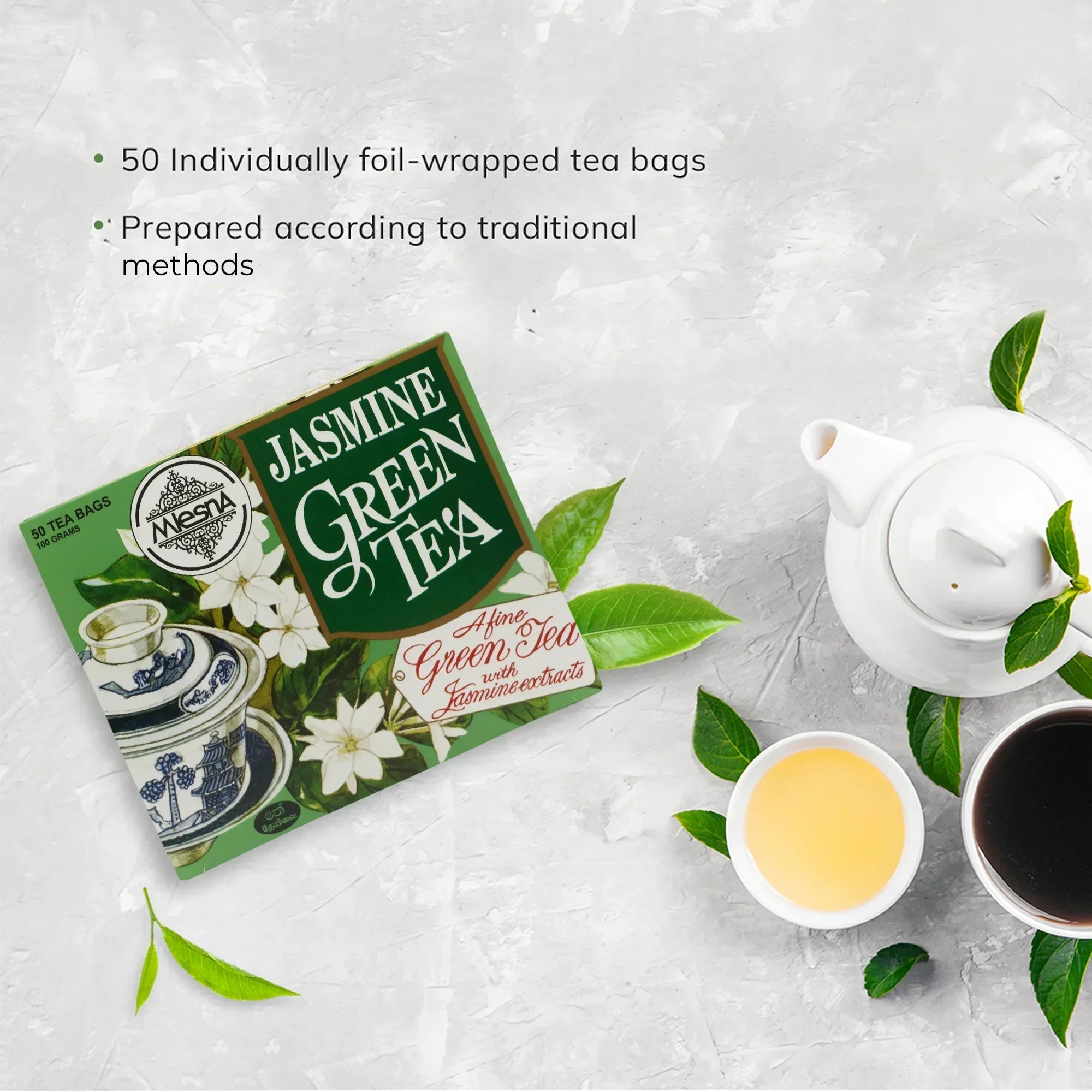 Jasmine green tea box, white teapot, two cups of tea, and green tea leaves on light background
