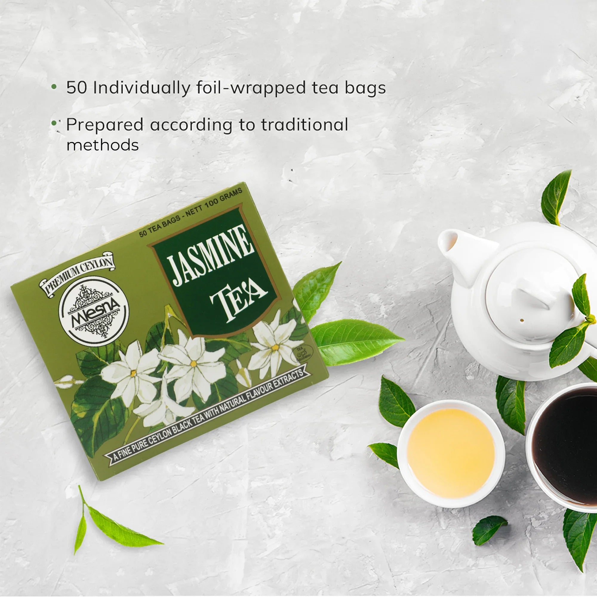 Jasmine tea box with Ceylon tea bags, teapot, green tea leaves, and tea cups on light surface