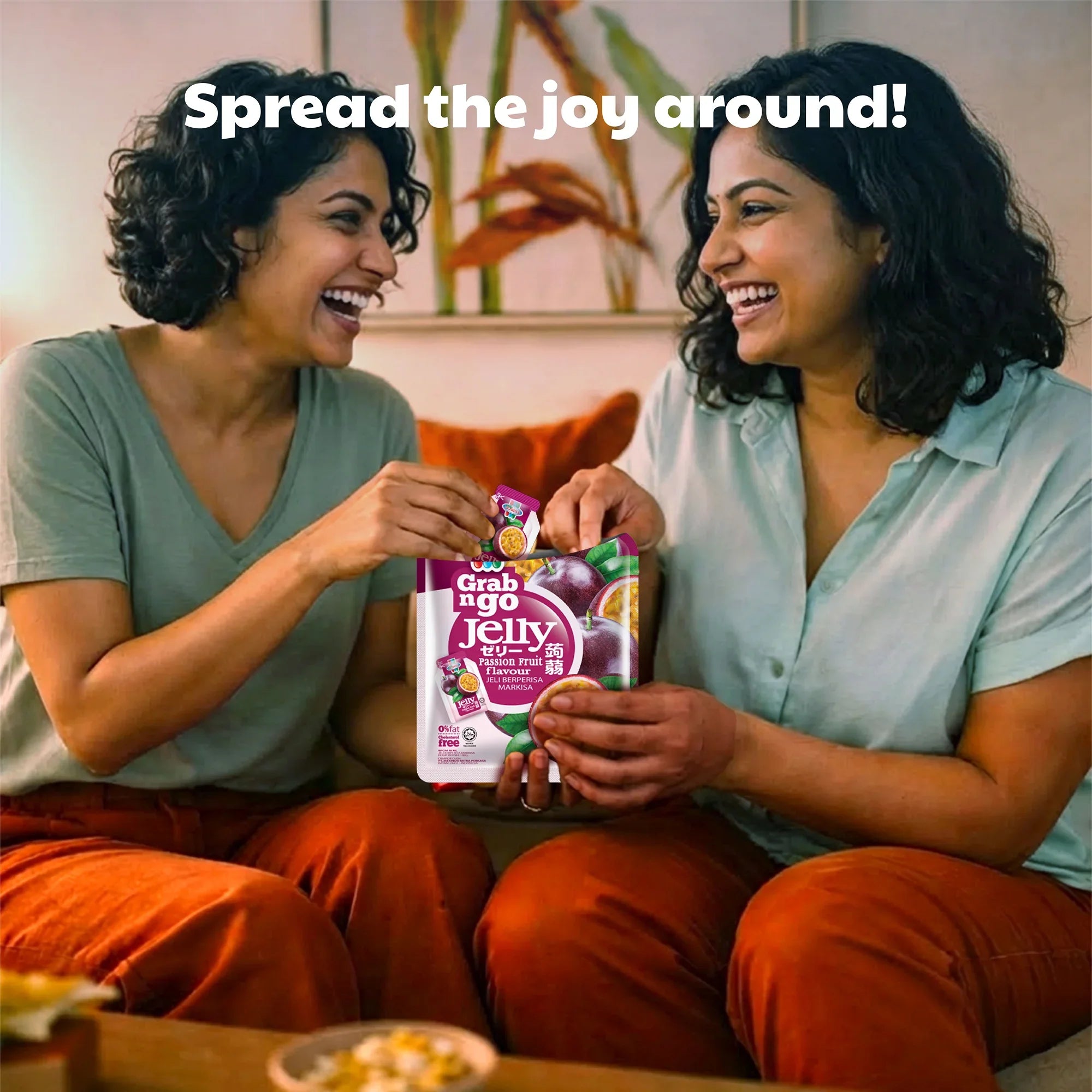 Two women smiling and sharing Grab n Go Passion Fruit Jelly snacks in a cozy living room.