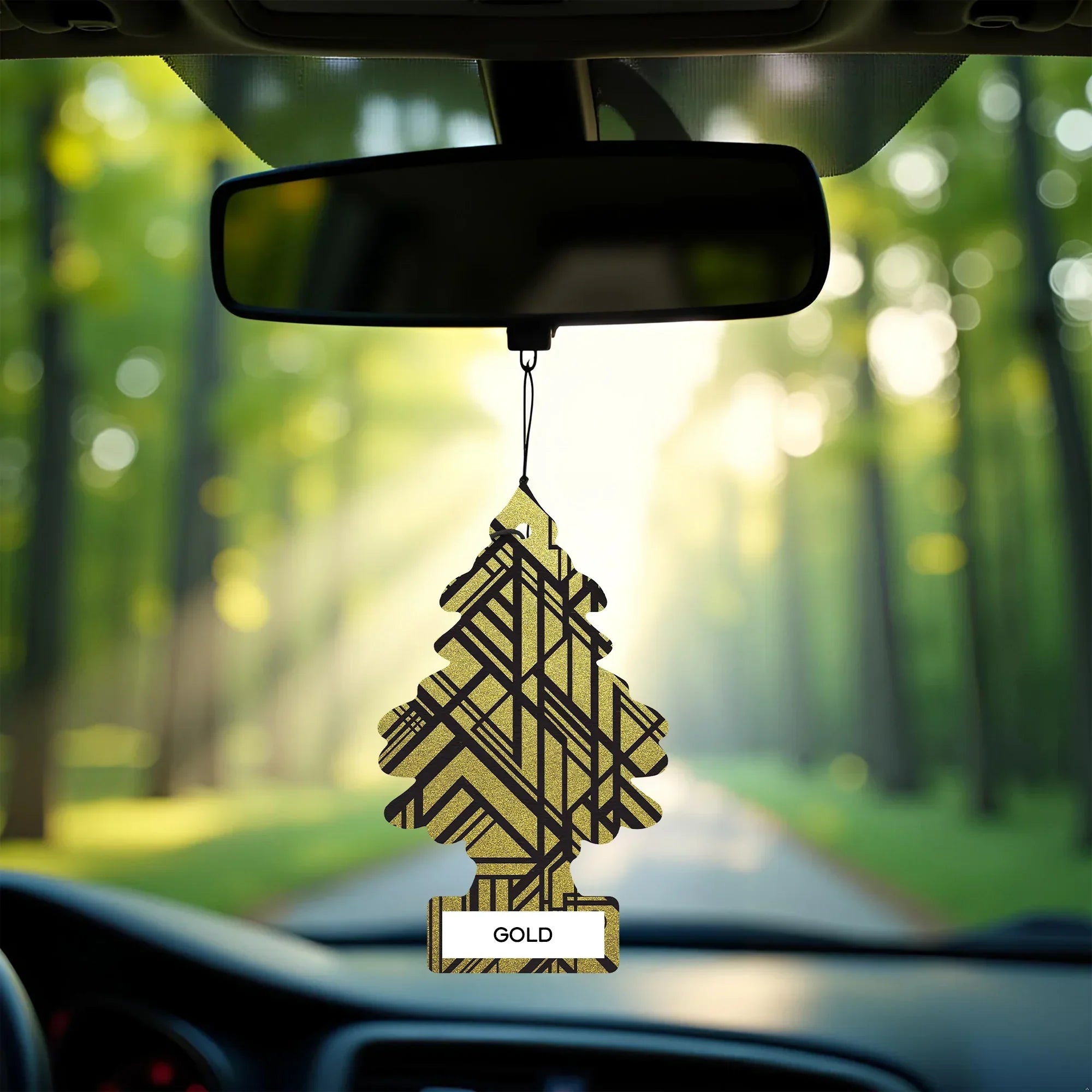 Gold Little Trees car air freshener hanging on rearview mirror, forest drive background
