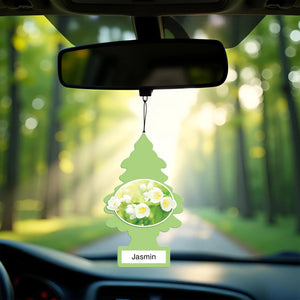 Little Trees Jasmin car air freshener hanging from rearview mirror with blurred green forest background