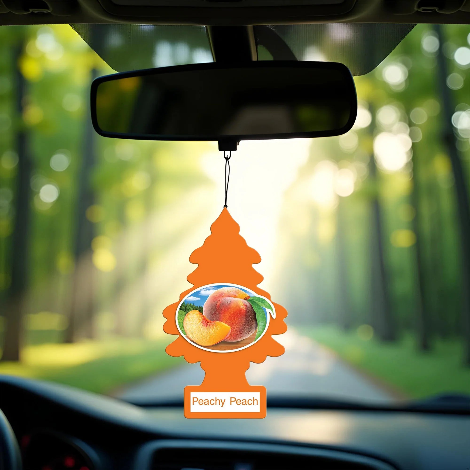 Peachy Peach scented Little Trees air freshener hanging from car rearview mirror with blurred forest background