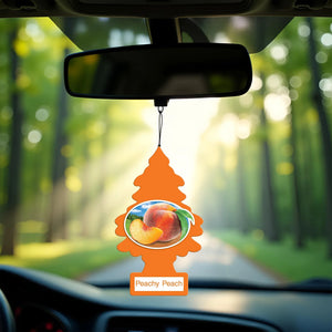 Peachy Peach scented Little Trees air freshener hanging from car rearview mirror with blurred forest background