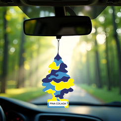 Colorful blue and yellow Little Trees Pina Colada car air freshener hanging from rearview mirror with sunlit forest road background