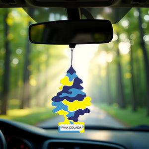 Colorful blue and yellow Little Trees Pina Colada car air freshener hanging from rearview mirror with sunlit forest road background