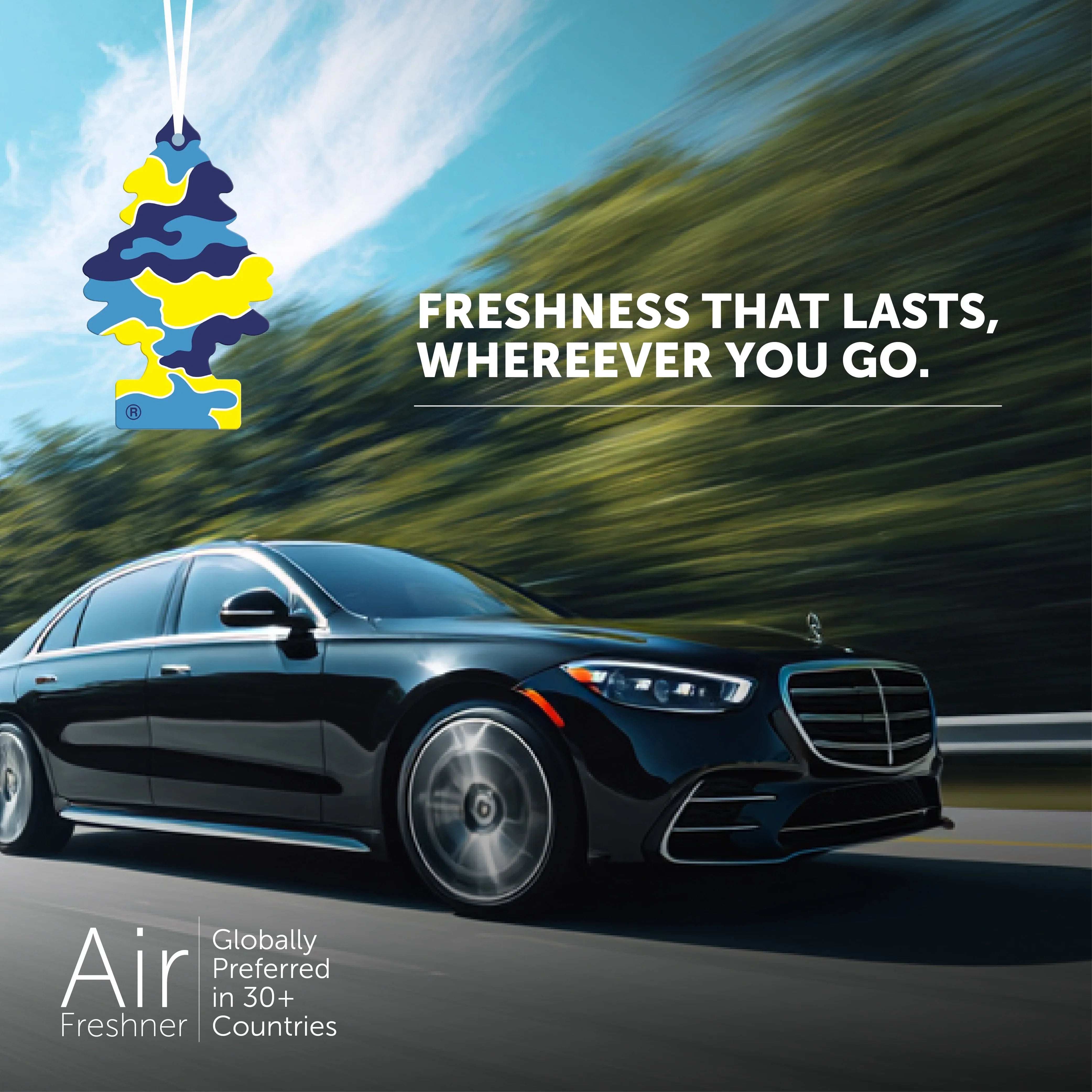 Black luxury car driving on road with blue sky and trees, featuring hanging camo-patterned air freshener