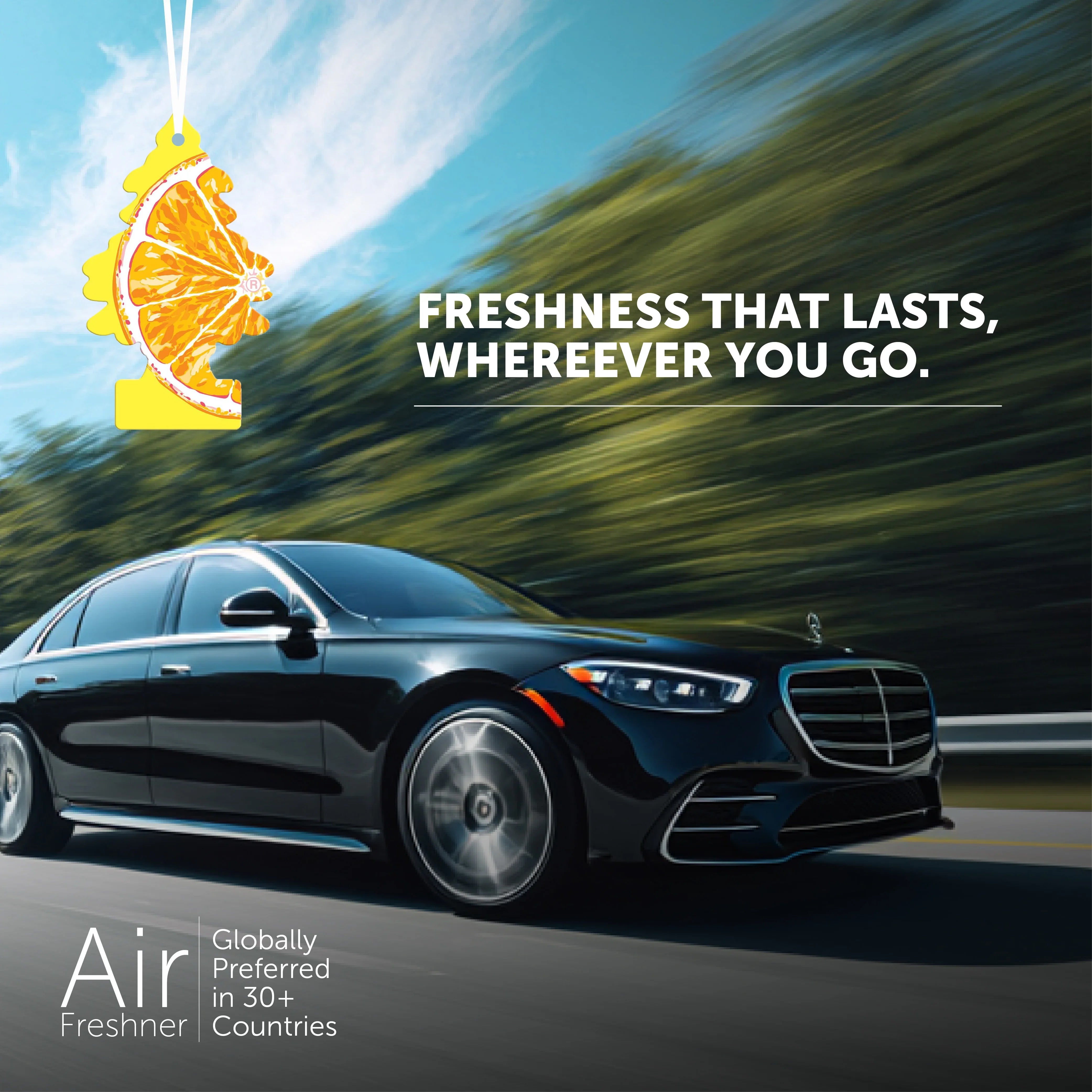 Little Trees sliced orange air freshener hanging in luxury black car driving on road with freshness tagline