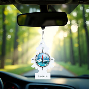 Little Trees True North car air freshener hanging from rearview mirror with forest and sunlight background