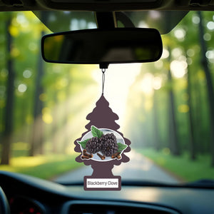 Blackberry Clove scented pine tree car air freshener hanging from rearview mirror with blurred forest background