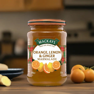 Jar of Mackays Orange Lemon & Ginger Marmalade on wooden surface with fresh oranges and ginger in background