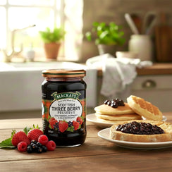 Jar of Scottish three berry preserve with berries, toast, and pancakes in a kitchen setting