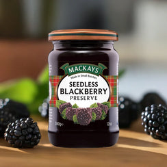 Jar of Mackays Seedless Blackberry Preserve with fresh blackberries on wooden surface