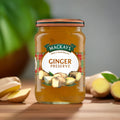 Jar of Mackays Ginger Preserve with fresh ginger roots on wooden surface