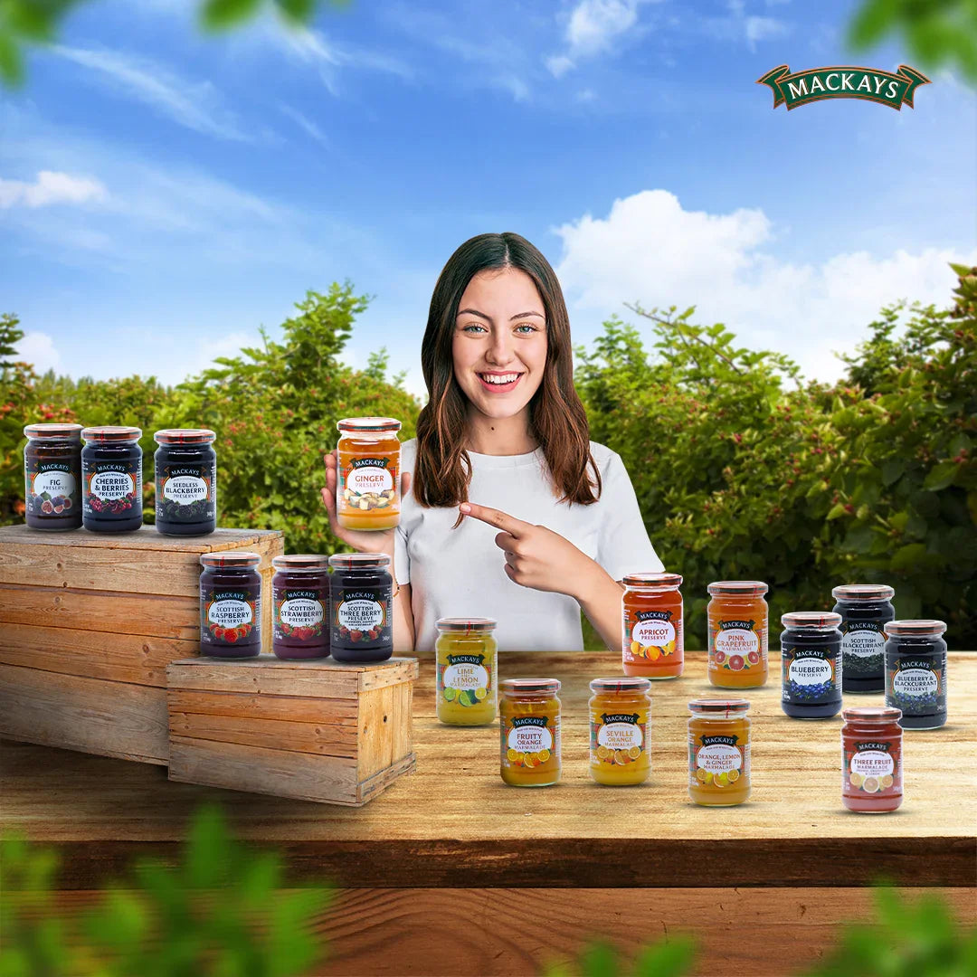 Smiling woman showcasing Mackays preserves and marmalades jars arranged on wooden crates outdoors