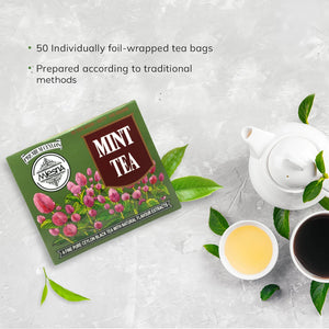 Box of mint tea with floral design beside teapot, teacups, and fresh green tea leaves