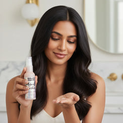 Woman with long dark hair holding Umberto Giannini Miracle Worker Smooth Serum bottle in a bright bathroom