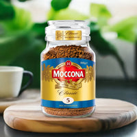 Moccona decaffeinated instant coffee jar on a wooden coaster with a blurred green background