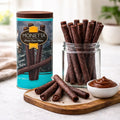 Chocolate cream wafer sticks in glass jar with tin can and creamy dip on wooden board