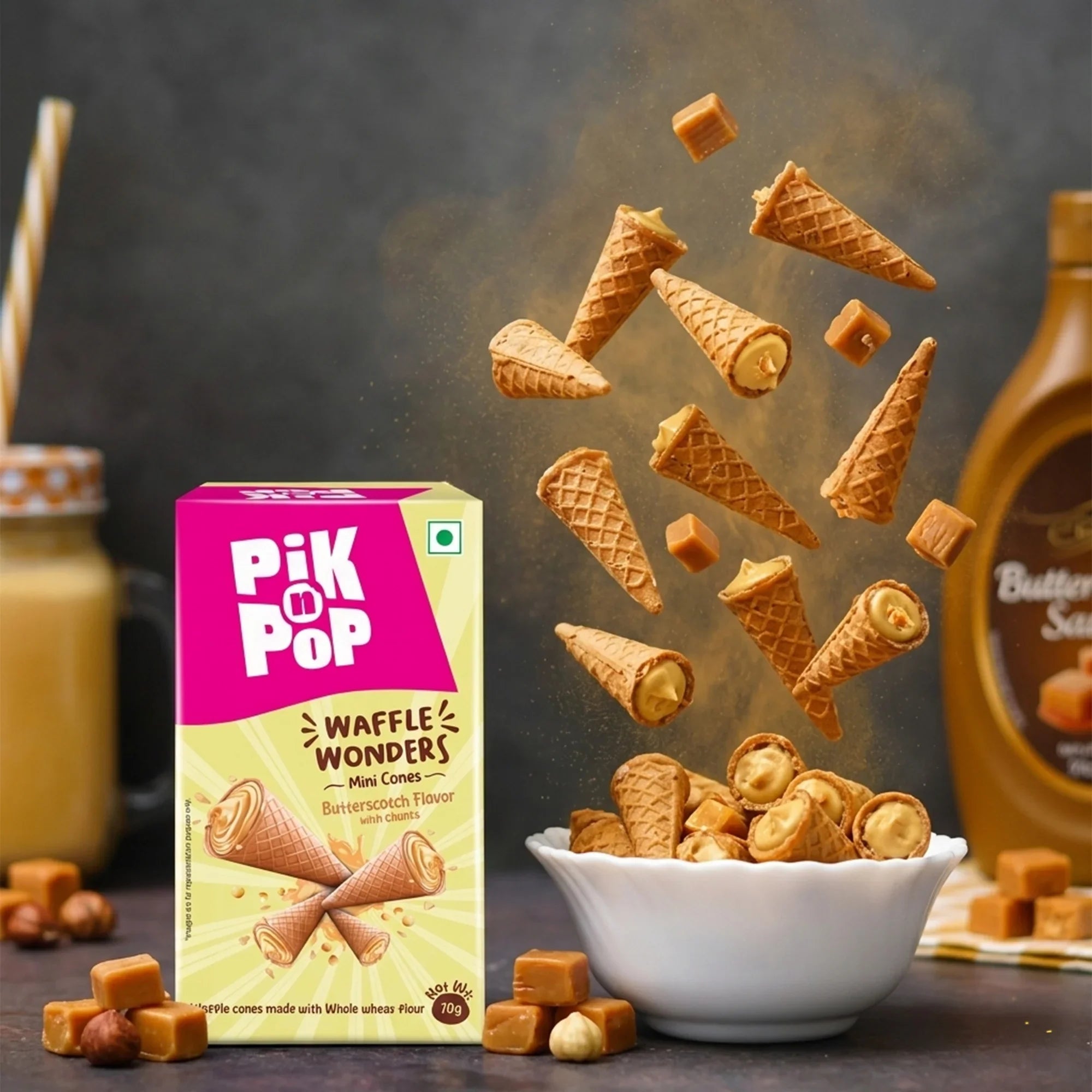 Mini butterscotch waffle cones with caramel chunks, box, and sauce bottle on a table.