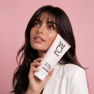 Woman holding a tube of Repair My Hair hair mask against a pink background.
