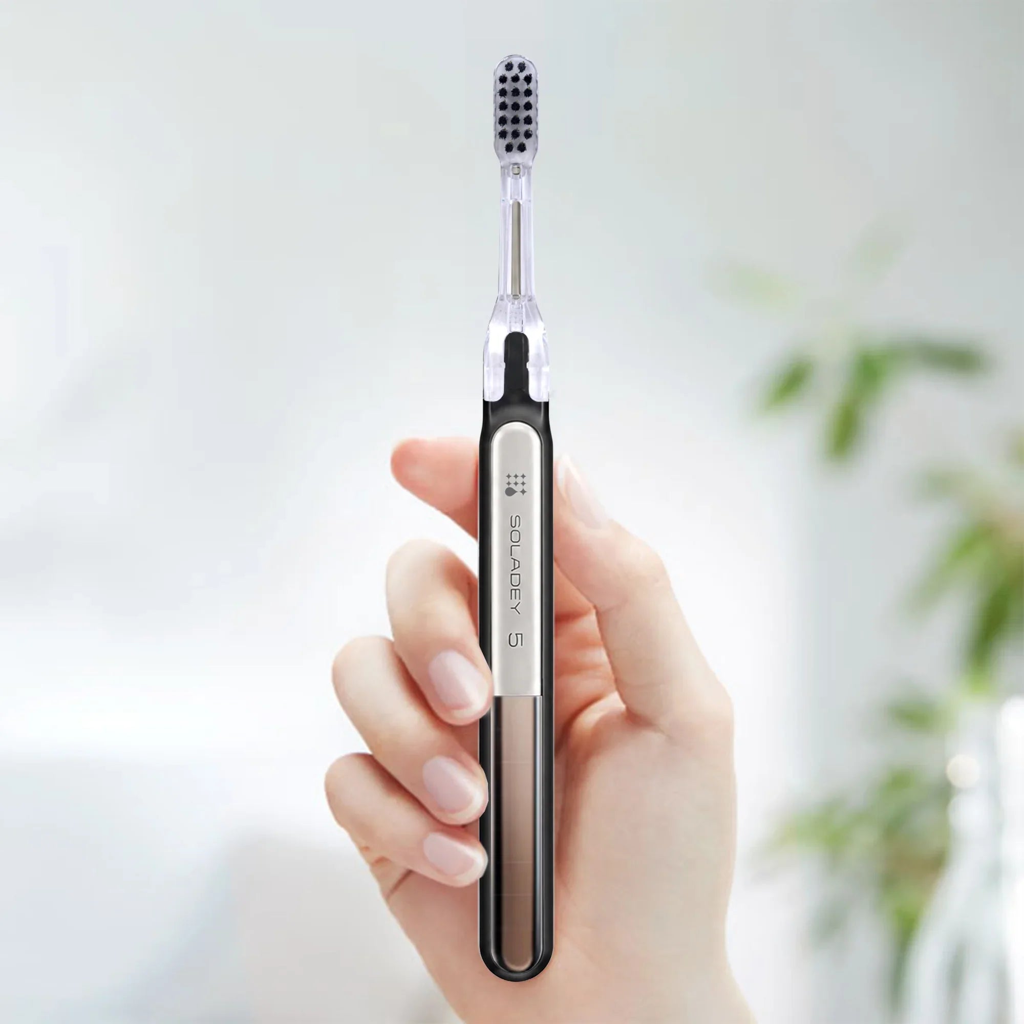 A hand holding a sleek Soladey 5 electric toothbrush with a silver and black handle.
