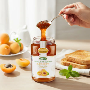 Hand scooping Stute no sugar added apricot jam from jar with fresh apricots, toasted bread, and mint on table