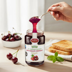Jar of Stute No Sugar Added Morello Cherry jam with spoonful of jam, fresh cherries in bowl, toast, and mint on wooden table