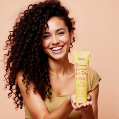 Smiling woman with curly hair holding Umberto Giannini Banana Coconut Air-Dry Styling Cream in yellow tube