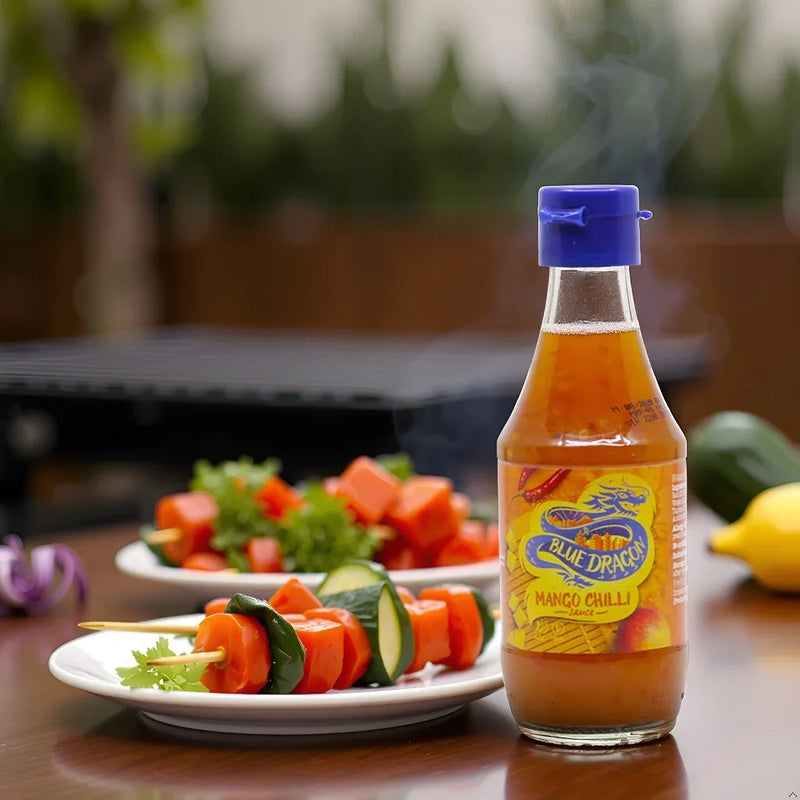 Blue Dragon mango chili sauce bottle with steaming vegetable skewers on plates outdoors