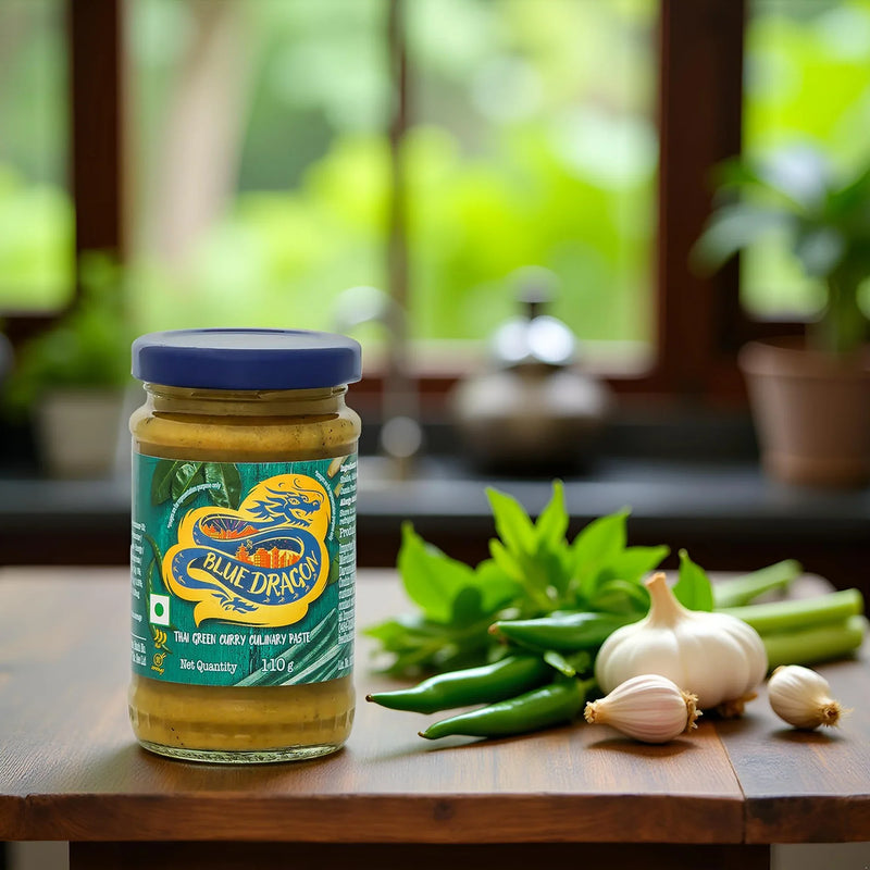 Jar of Blue Dragon Thai green curry paste with fresh green chili, garlic, and herbs on wooden table