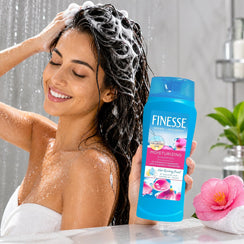 Woman washing hair with Finesse Moisturizing Shampoo under shower, featuring hyaluronic acid for soft, manageable hair