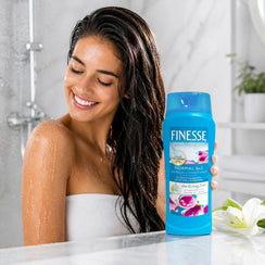 Woman in shower holding Finesse Normal 2-in-1 Shampoo + Conditioner with hyaluronic acid for shine & manageability