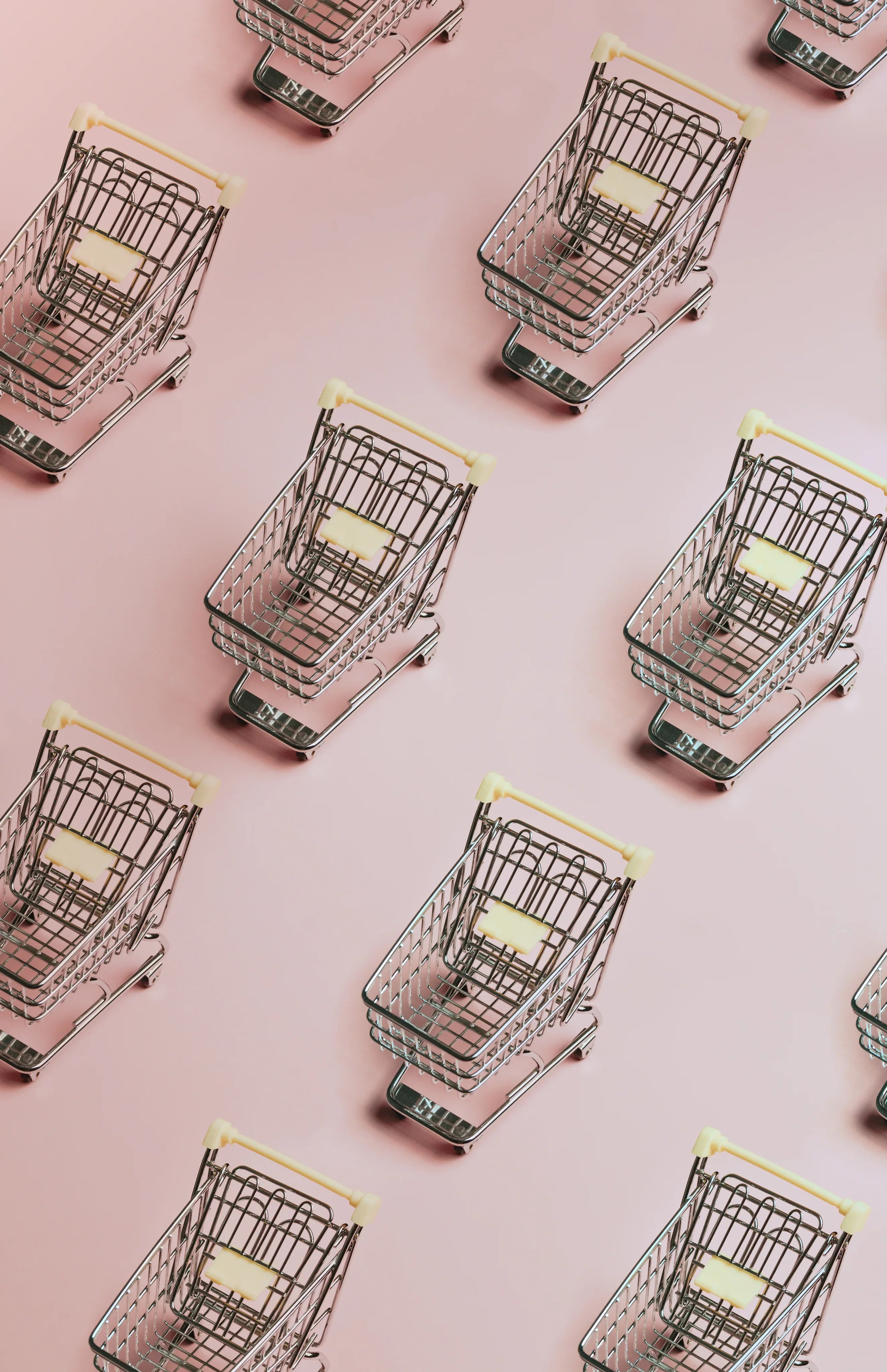 Pattern of silver miniature shopping carts with beige handles on a pastel pink background