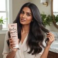 Woman with long smooth black hair holding Umberto Giannini Salon Smooth smoothing conditioner in bright bathroom
